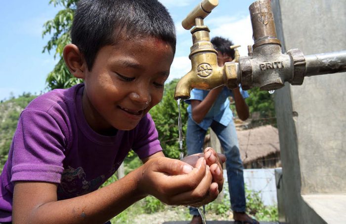 Un bambino beve dell'acqua da un rubinetto in Nepal